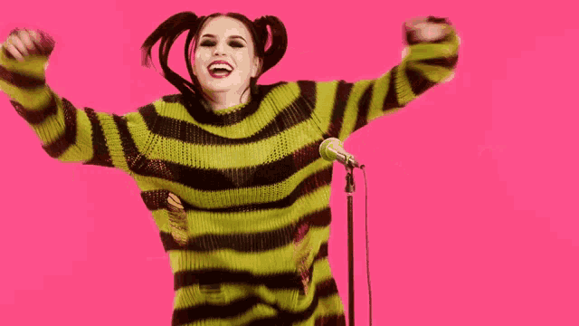a woman in a yellow and black striped sweater is singing into a microphone