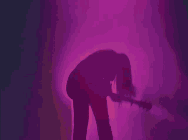 a silhouette of a person playing a guitar in front of a pink light