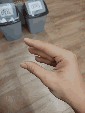 a person 's hand is reaching for a trash can that says paper