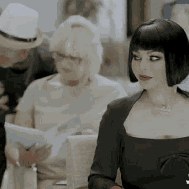 a woman in a black dress is sitting at a table with a man in a hat .