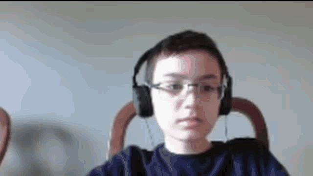 a young boy wearing headphones and glasses is sitting in a chair and looking at the camera .