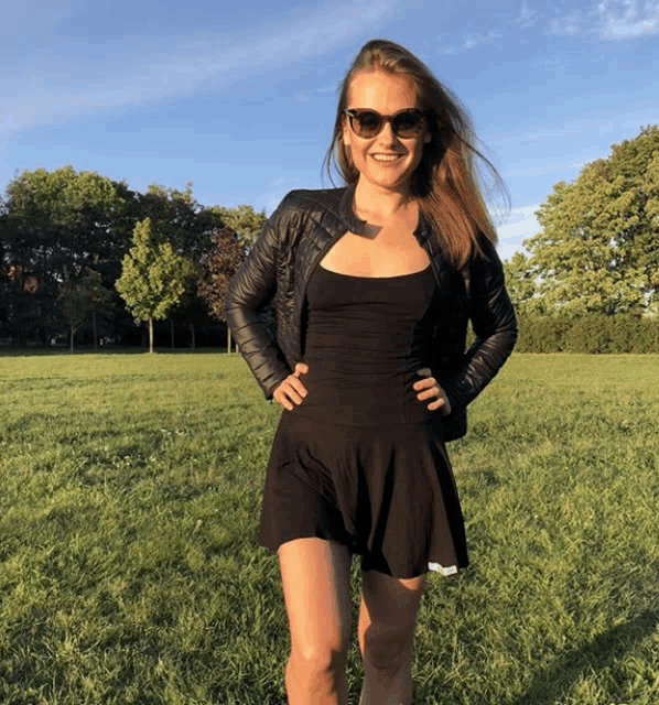 a woman in a black dress and sunglasses stands in a field