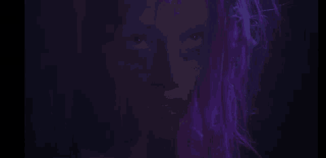 a woman with purple hair is looking at the camera in the dark .