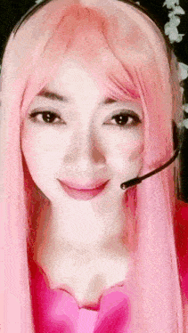 a woman wearing a pink wig and a headset smiles for the camera