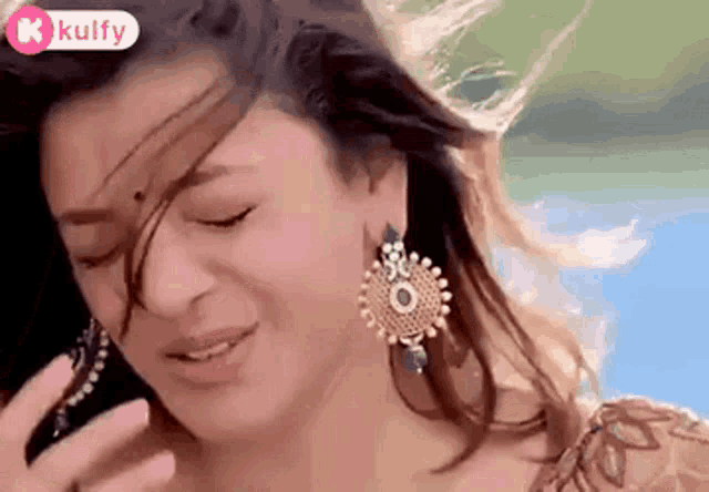 a woman wearing earrings is talking on a cell phone with her hair blowing in the wind .