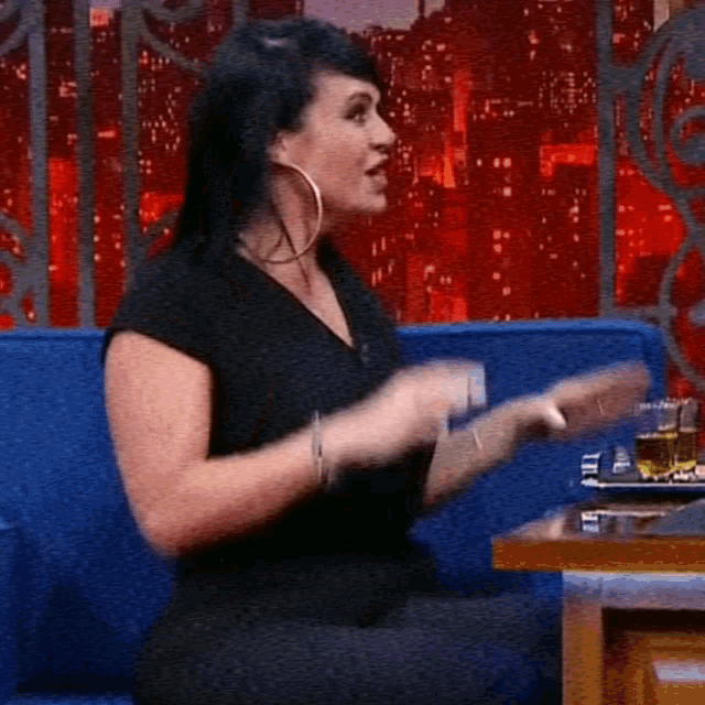 a woman in a black shirt is sitting on a blue couch talking
