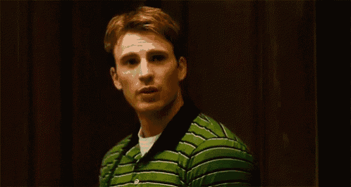a young man wearing a green striped shirt is standing in a dark room .
