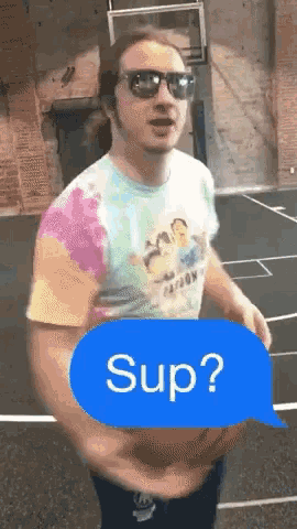 a man wearing sunglasses and a tie dye shirt is standing on a basketball court with a text bubble that says sup