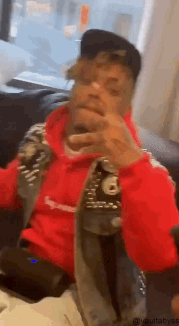 a man in a red hoodie and hat is sitting on a couch .