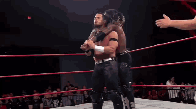 two wrestlers are hugging each other in a ring with a referee