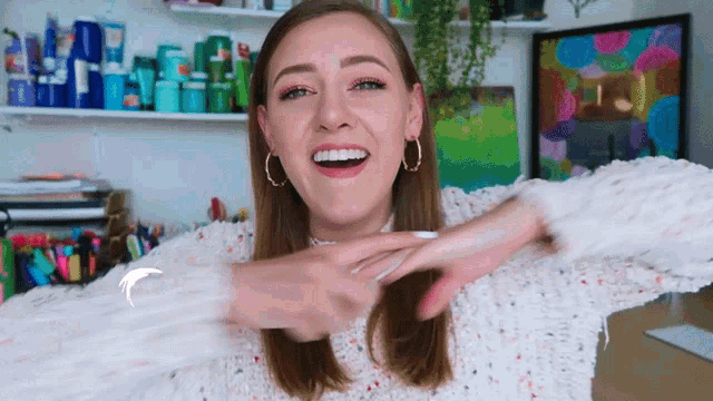 a woman wearing a white sweater and hoop earrings is smiling and pointing