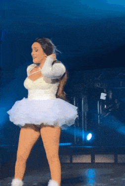 a woman in a white dress is singing into a microphone on stage