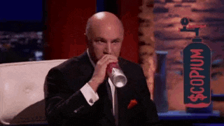 a man in a suit is drinking from a cup with a bottle of scopium in the background