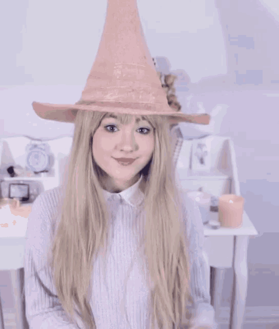 a woman wearing a pink witch hat holds a pink candle