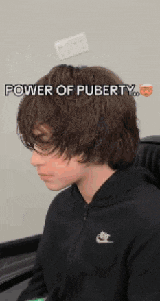 a young boy with long hair is wearing a black nike sweatshirt .