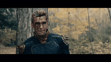 a man with blood on his face is standing next to a tree in the woods .