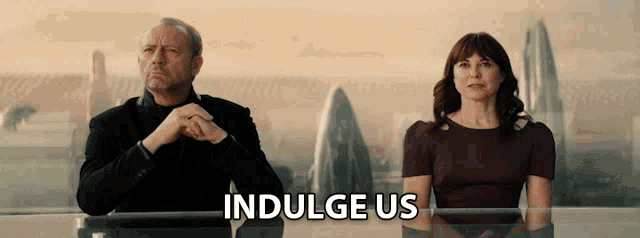a man and a woman are sitting next to each other with the words indulge us behind them