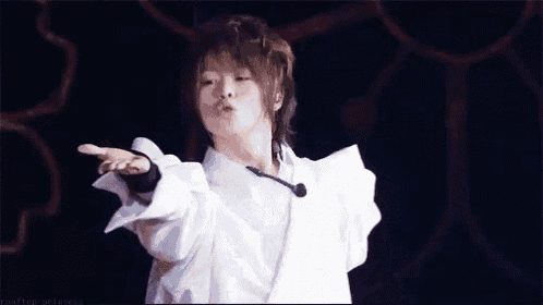 a young man wearing a white shirt and a microphone is making a peace sign .