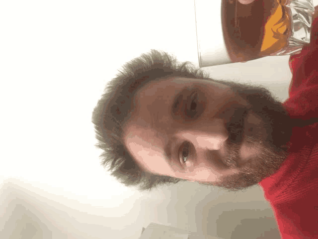 a man with a beard wearing a red sweater is looking at the camera