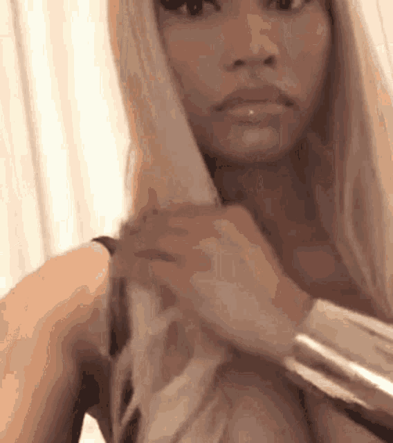 a woman with long blonde hair is taking a selfie with her hair blow dryer .