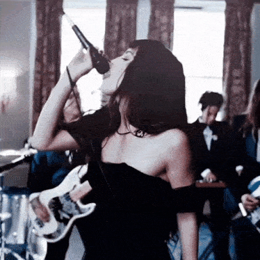 a woman in a black dress singing into a microphone with a guitar in the background