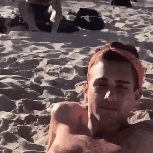 a shirtless man is laying on the beach with a headband on his head .