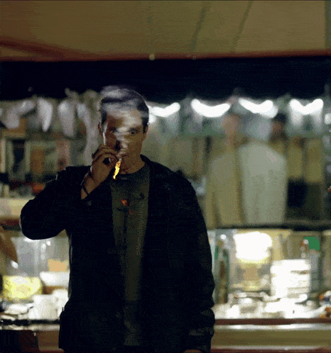a man in a black jacket is smoking a cigarette in front of a counter