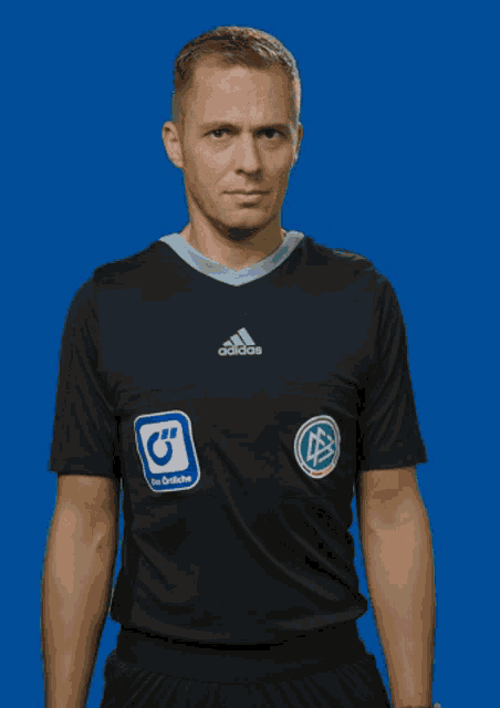 a man wearing a black adidas shirt has a blue sticker on his pocket