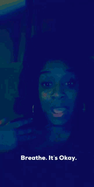a woman in a dark room with the words breathe it 's okay below her
