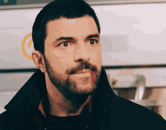 a man with a beard and a black jacket looks to the side