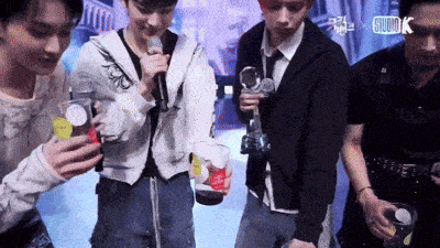 a group of young men are standing around holding cups and a microphone with the word studiok on the bottom