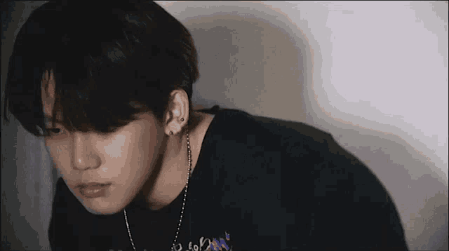 a close up of a young man wearing a black shirt and a necklace .