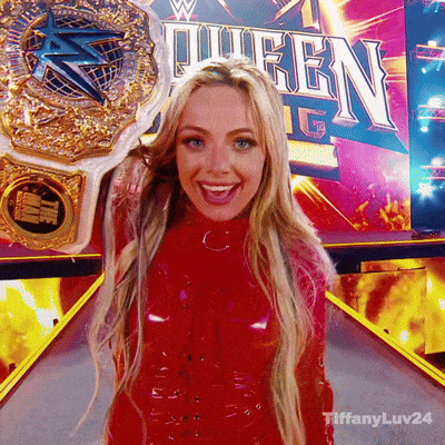 a woman in a red dress is holding a wrestling championship belt