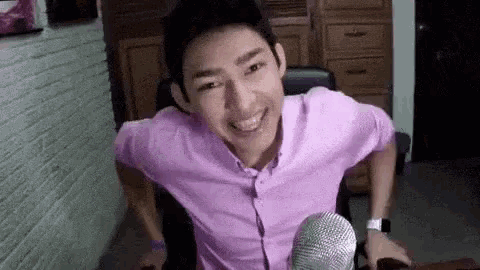 a man in a purple shirt is sitting in front of a microphone .