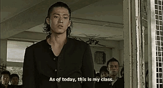 a man in a black suit is standing in front of a group of people in a classroom .