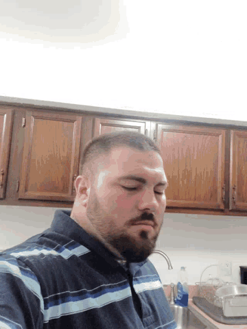 a man with a beard is sleeping in a kitchen with wooden cabinets