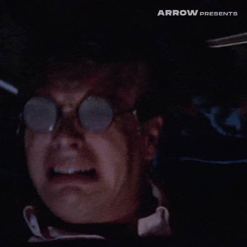 a man wearing round glasses and headphones is screaming in a car