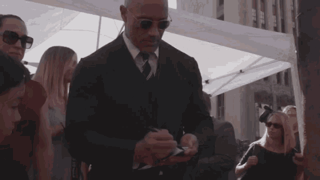 a man in a suit and tie is signing a piece of paper in front of a crowd .