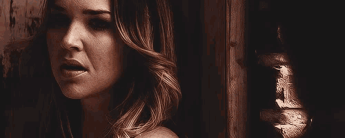 a close up of a woman 's face in a dark room with a reflection of a person in the wall .