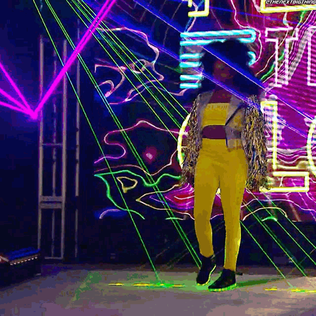 a woman in a yellow jumpsuit is standing in front of a neon sign