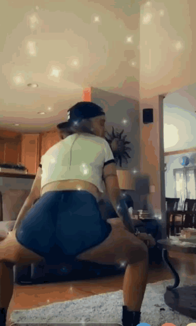 a woman in a white crop top and blue shorts is doing a squat in a living room