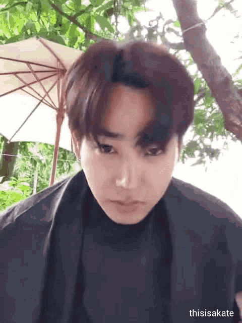 a young man is making a funny face in front of a tree and umbrella .