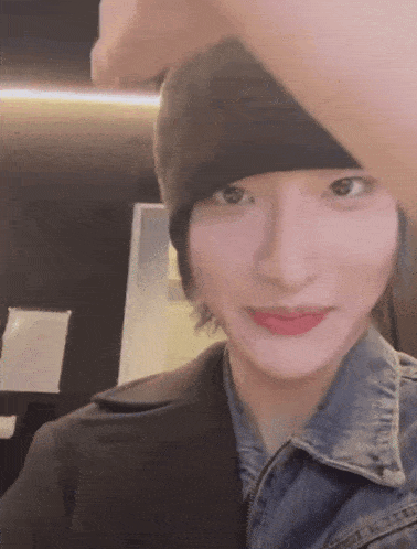 a woman wearing a beanie and a denim jacket is looking at the camera .