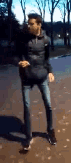 a man in a black jacket and jeans is dancing on a street .