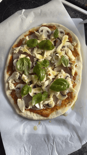 a pizza with mushrooms and basil on top is sitting on a piece of wax paper