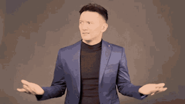 a man in a blue suit and black turtleneck is shrugging his shoulders