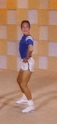 a man in a blue shirt and white shorts is dancing in front of a checkered wall