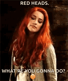 a woman with red hair is standing in front of a brick wall and looking down .