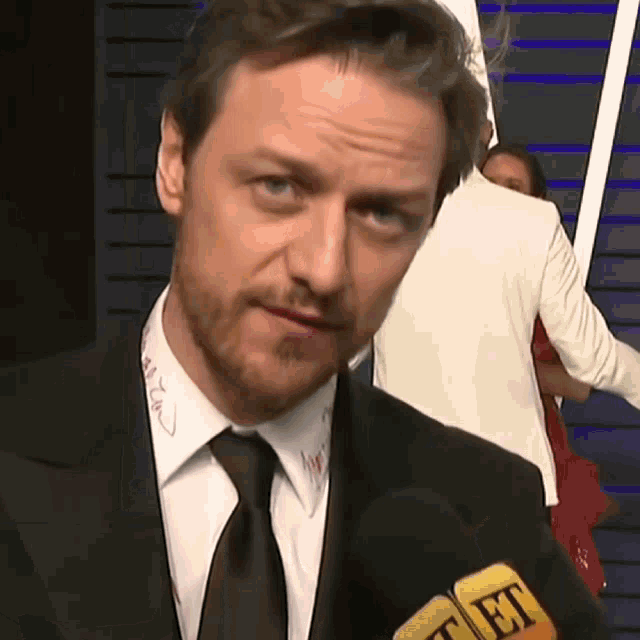 a man in a suit and tie is talking into a microphone with the word et on it