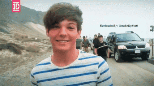 a young man wearing a striped shirt is smiling in front of a 1d logo and a car